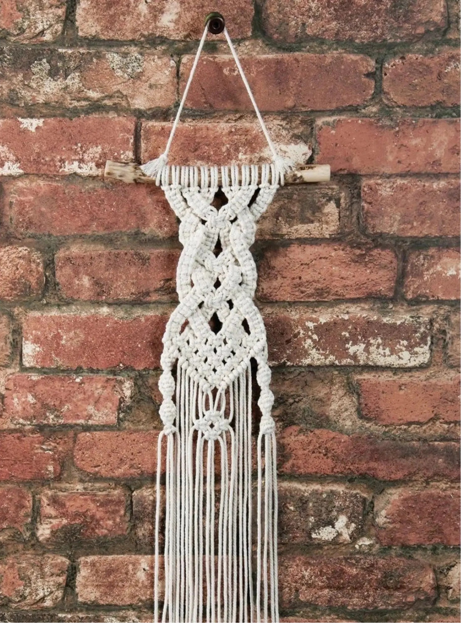 Macrame wall hanging with fringes against a brick wall