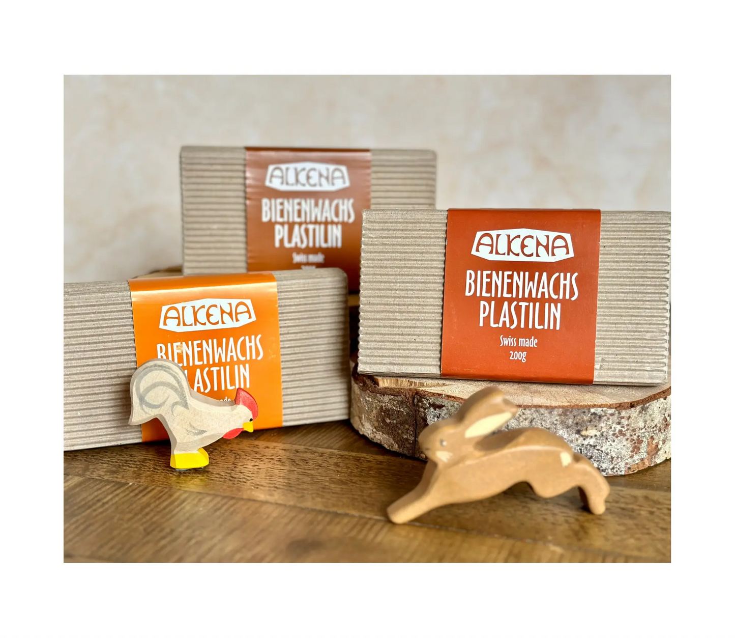 Packages of Alkena Beewax Playdough on a wooden surface with animal figurines.