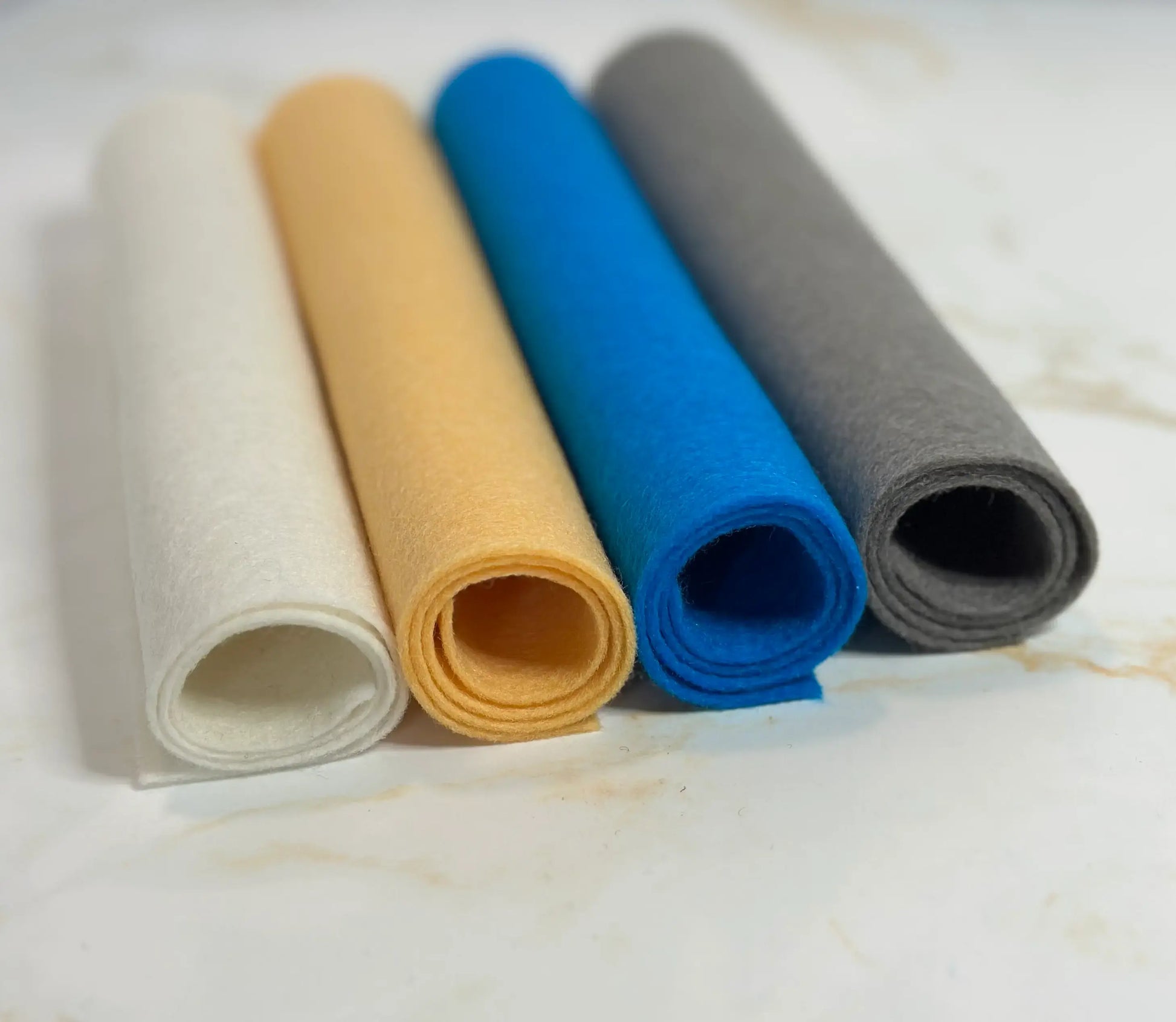 Four rolls of European Wool Felt Sheets in different colors on a marble surface