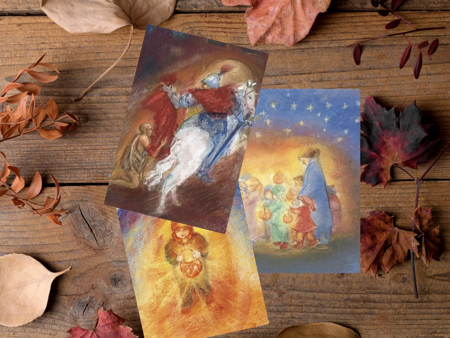 Three Martinmas cards on a wooden surface with autumn leaves.