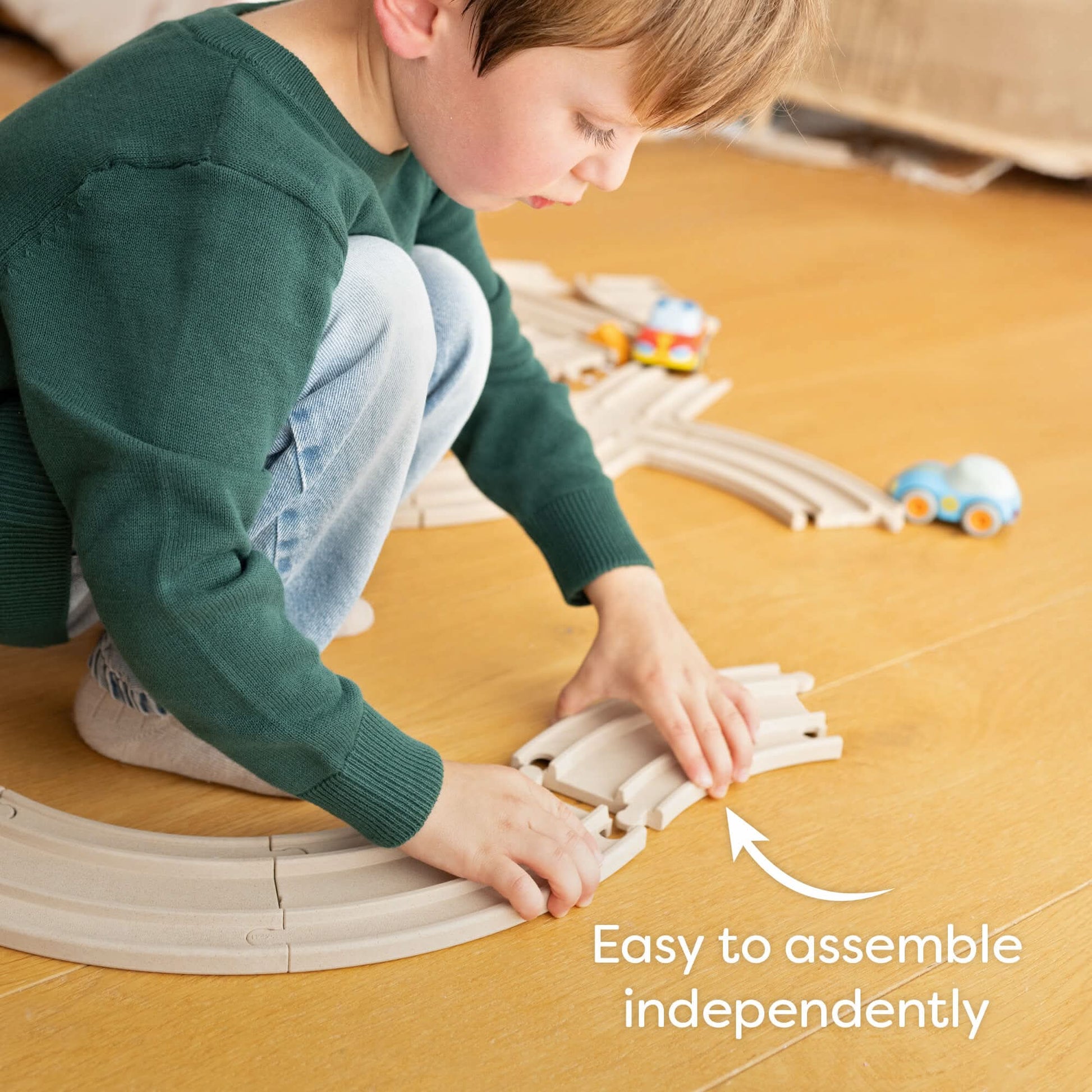 Child playing with a toy train set on a wooden floor