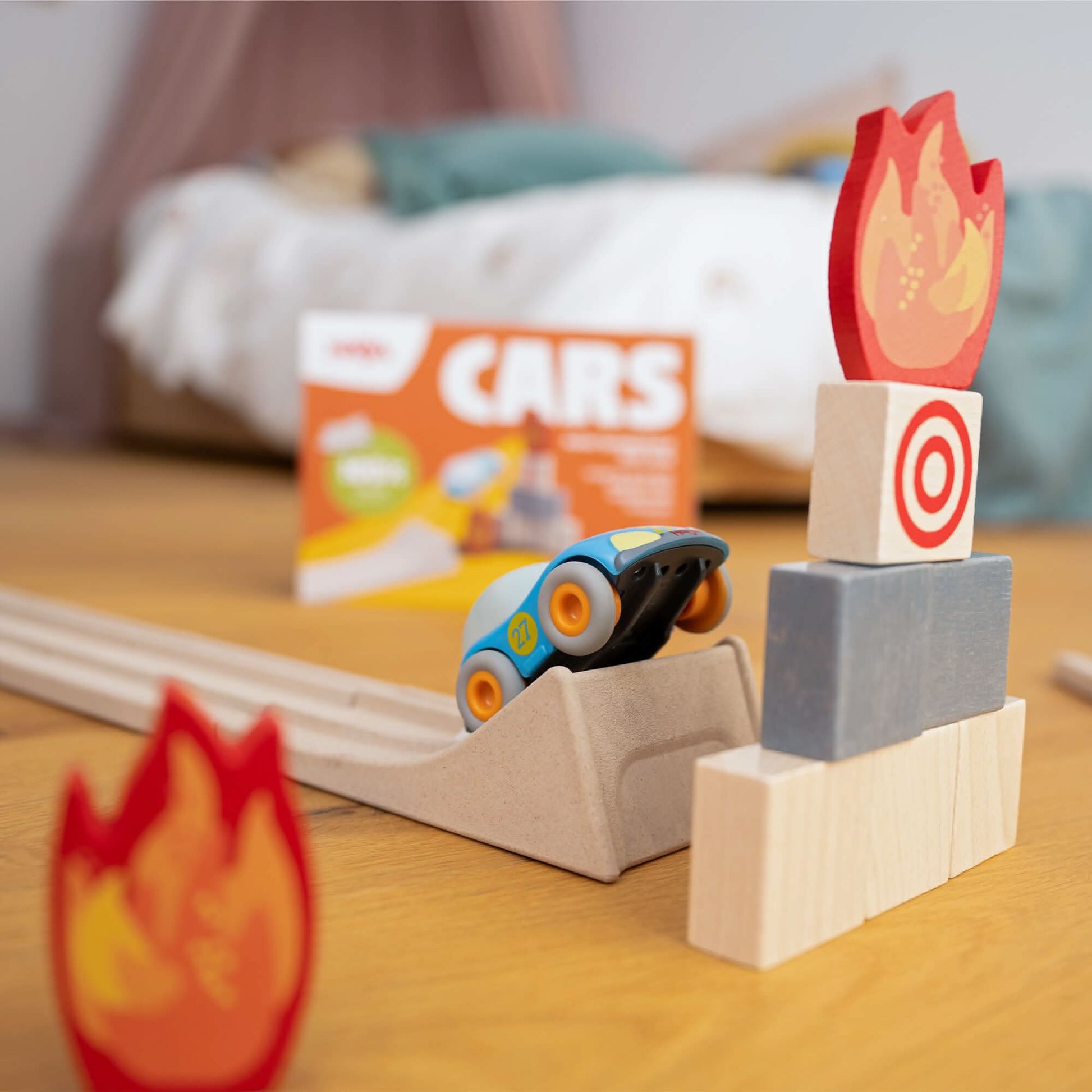 Toy car on a track with wooden blocks and fire-themed elements on a wooden surface.