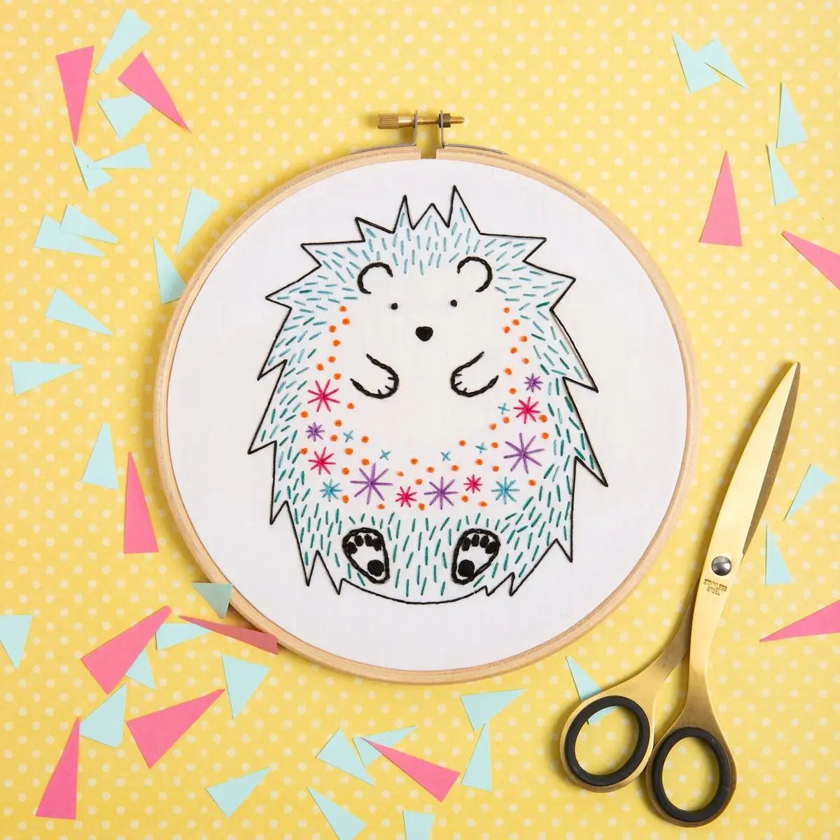 Embroidery hoop with a colorful hedgehog design on a yellow background with scissors.