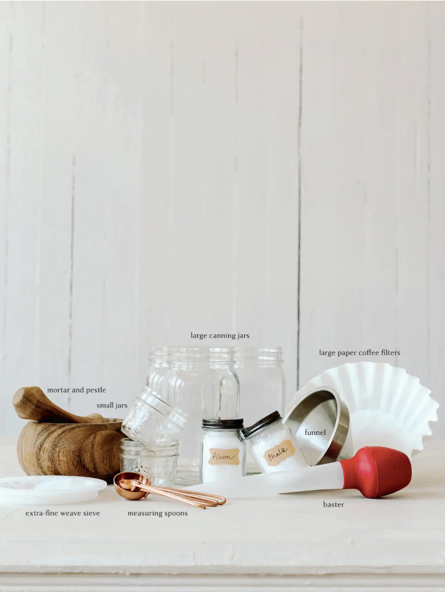 Set of kitchen utensils including jars, measuring spoons, and a funnel for making your own paints on a white surface.