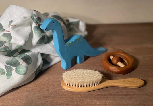 Natural Baby Brush next to a wooden rattle, baby toy and baby swaddle