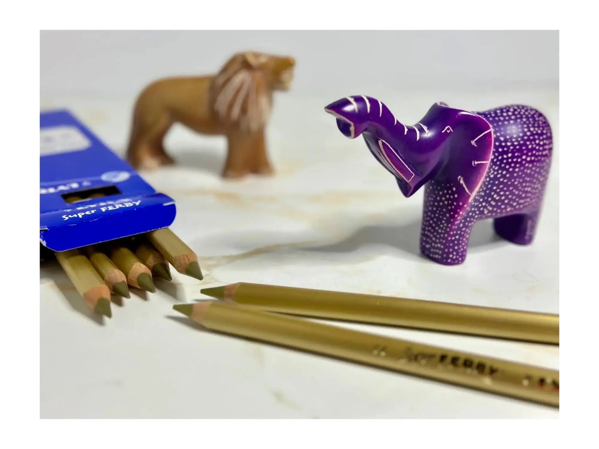 Pencils with a purple elephant-shaped sharpener and a toy lion on a white surface