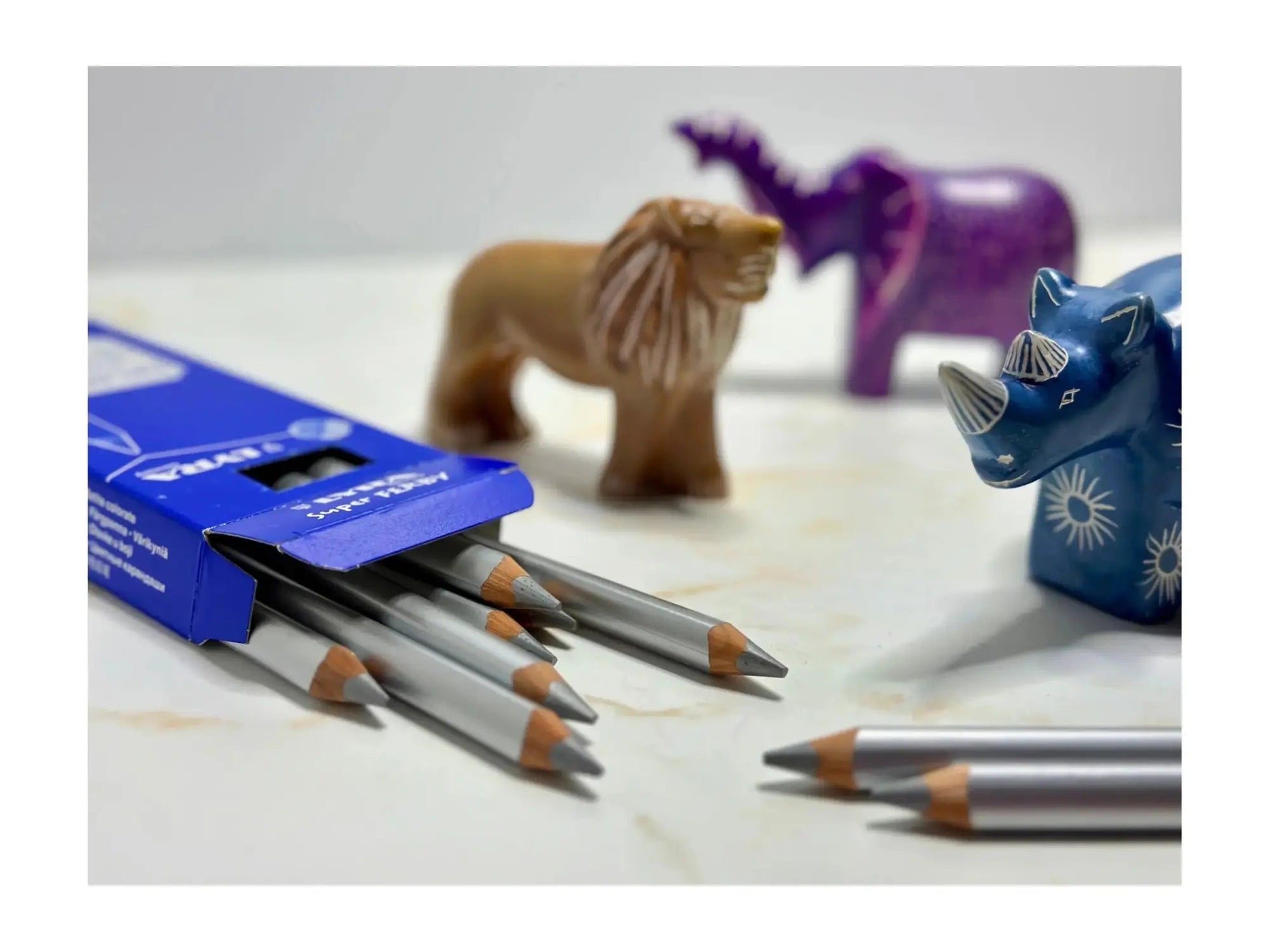 Set of pencils with a box on a surface with toy animals in the background