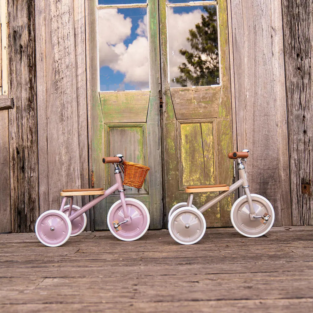 Banwood vintage trike toddler tricycles in dusty pink and beige in front of rustic wood doors