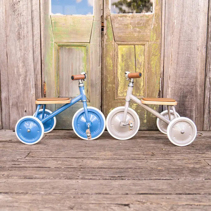 Banwood vintage trike toddler tricycles in blue and beige in front of rustic wood doors