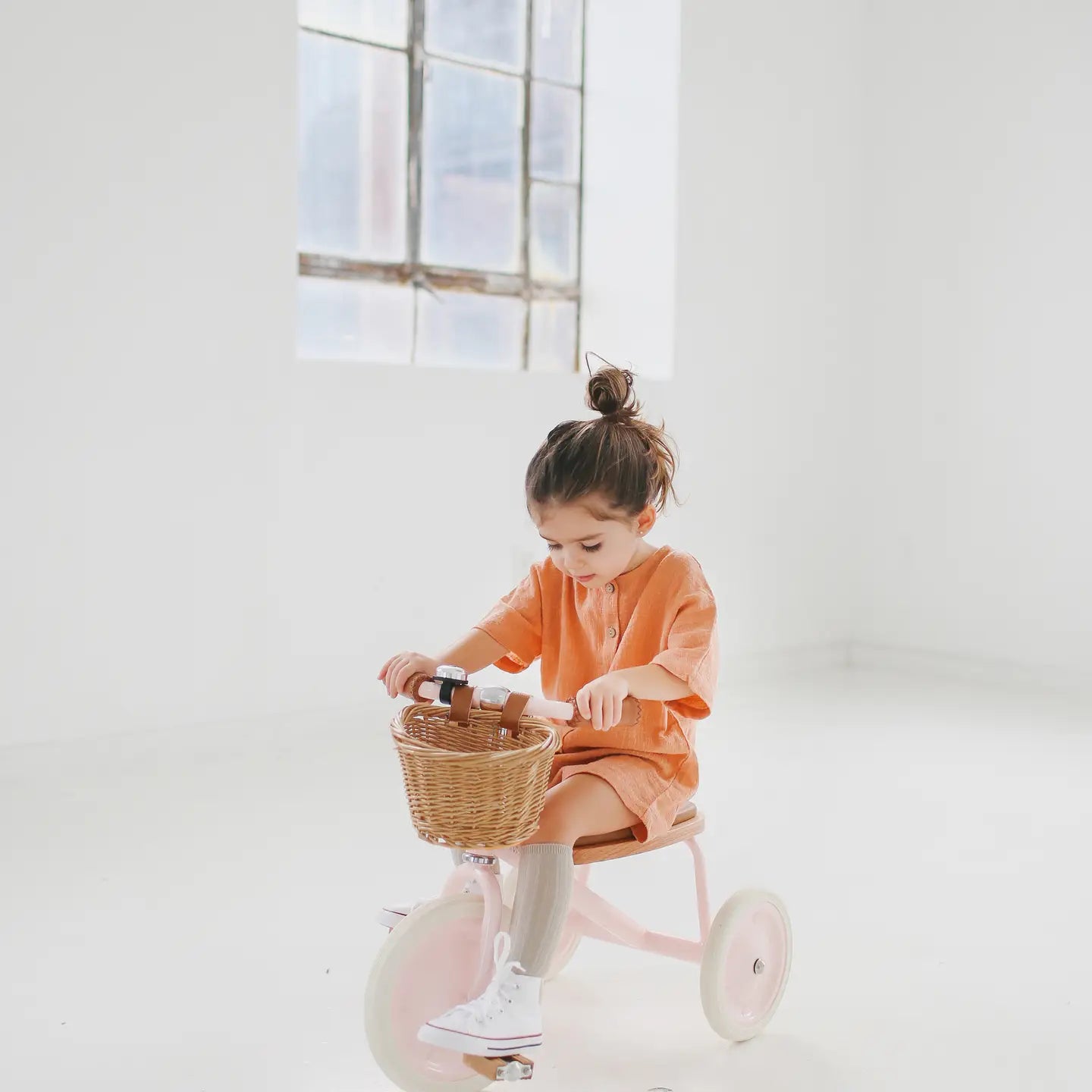 Child sitting on a tricycle with a basket in a bright room