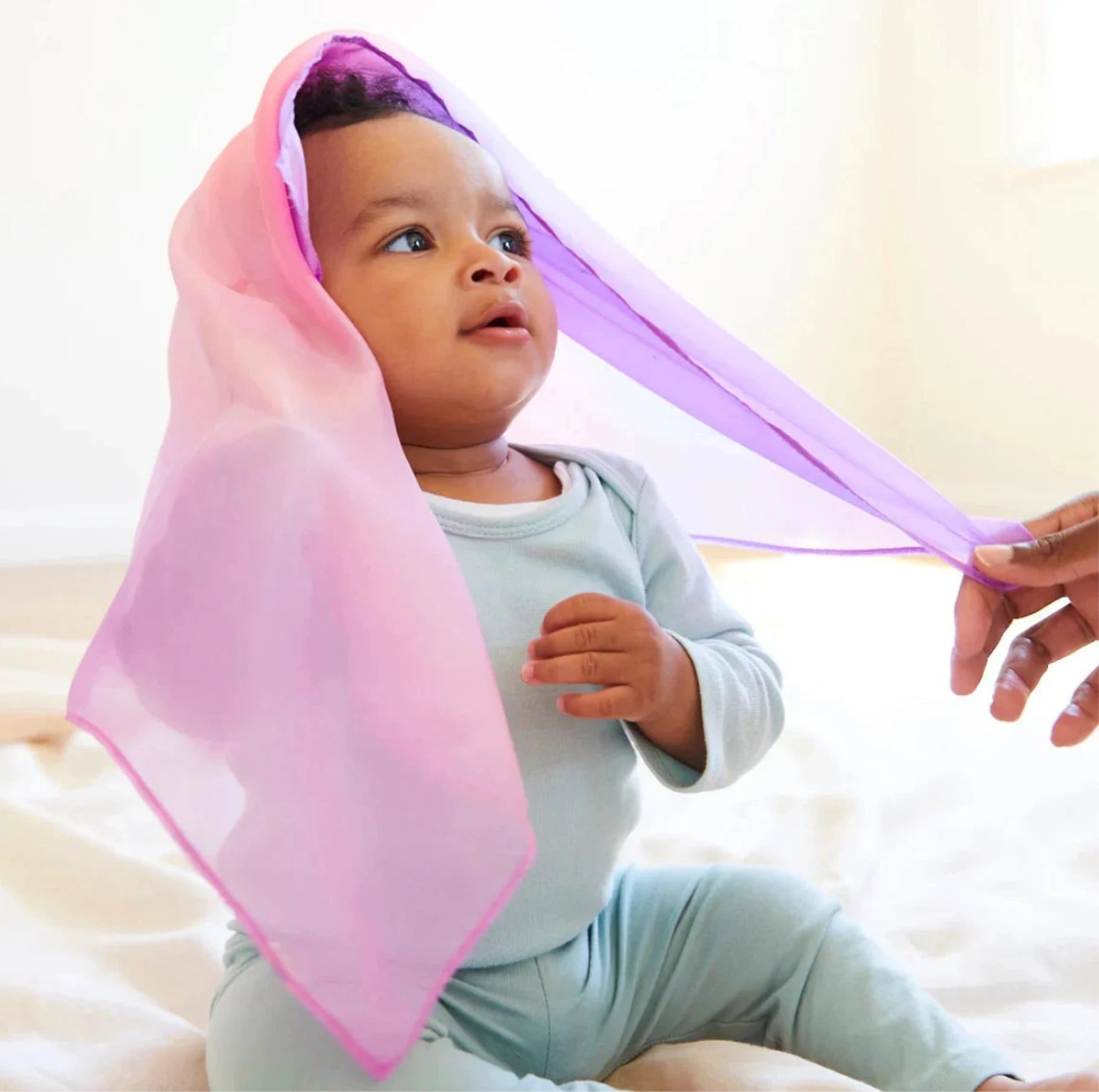 Sarah’s Silks - A baby playing with the Enchanted mini Playsilk in blossom