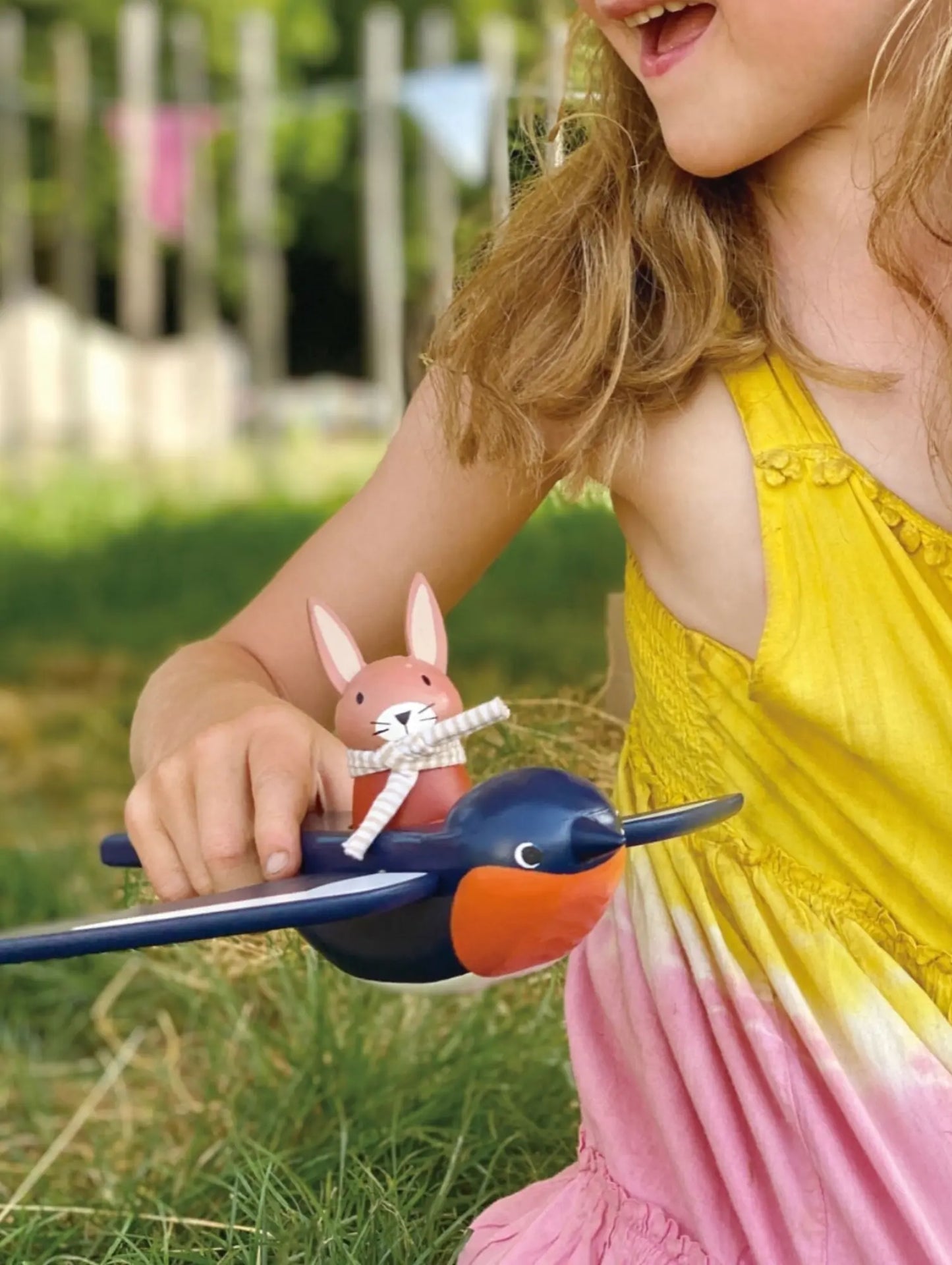 Child holding a toy bird with a rabbit figure outdoors