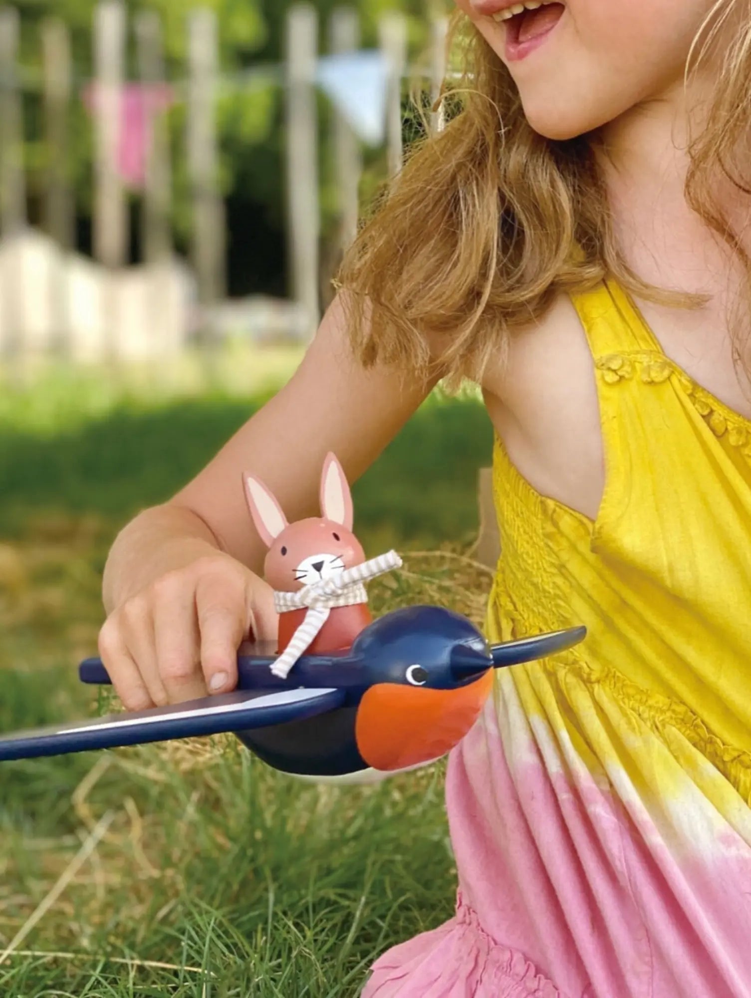 Child holding a toy bird with a rabbit figure outdoors