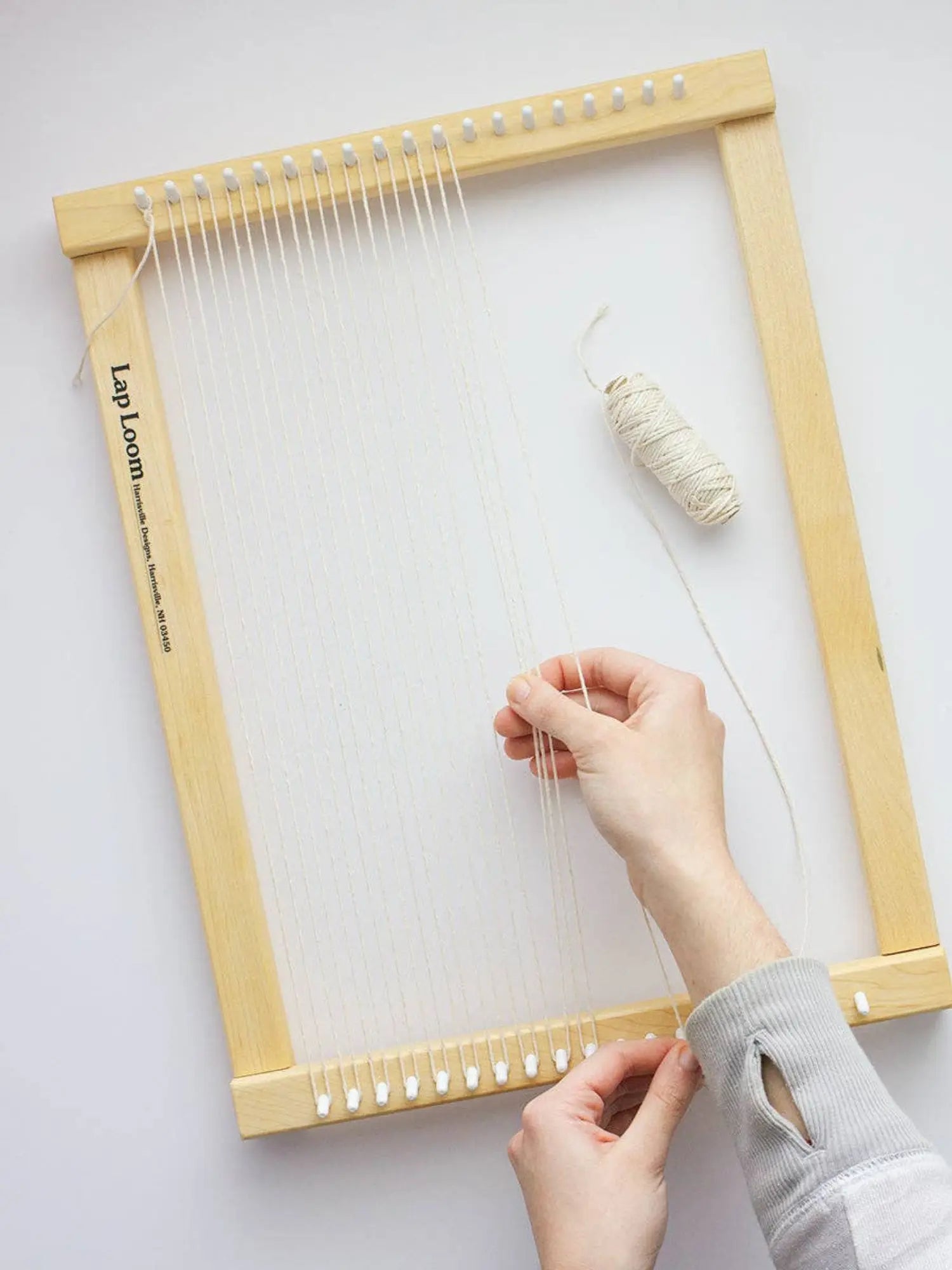 Person using a lap loom with yarn on a white background