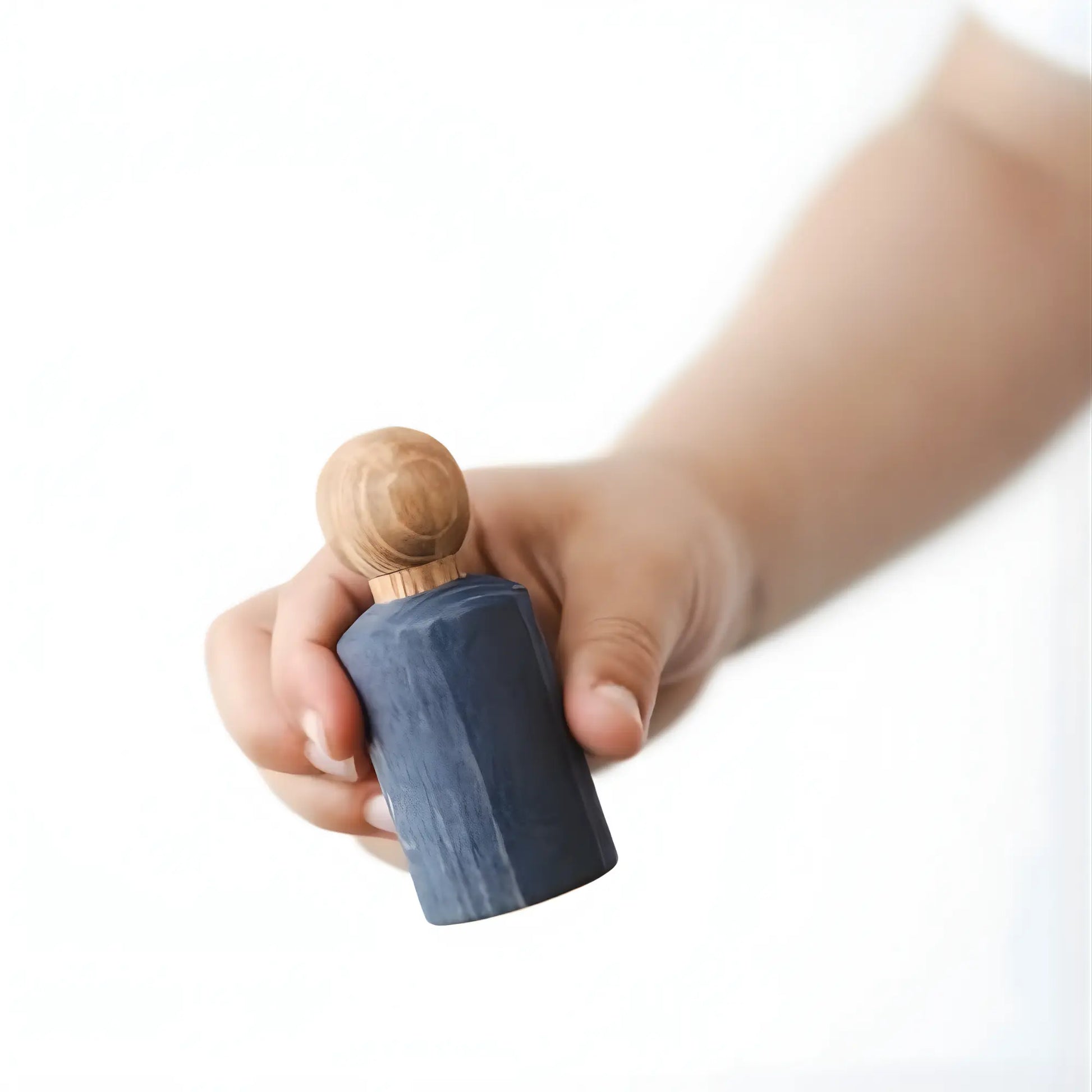 Hand holding a small blue jWaldorf inspired Blue stained peg doll  against a white background