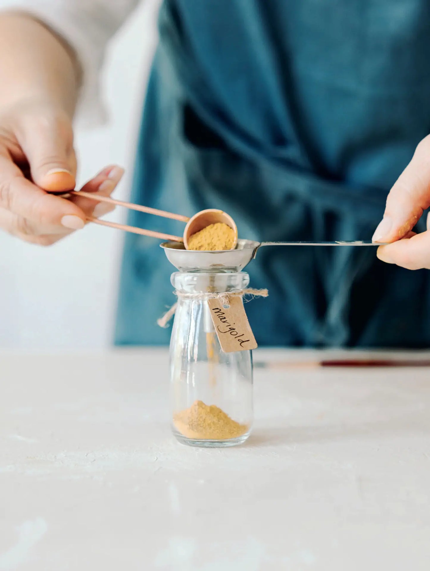 Person measuring and transferring a small amount of plant powder from a jar using a spoon to make paint