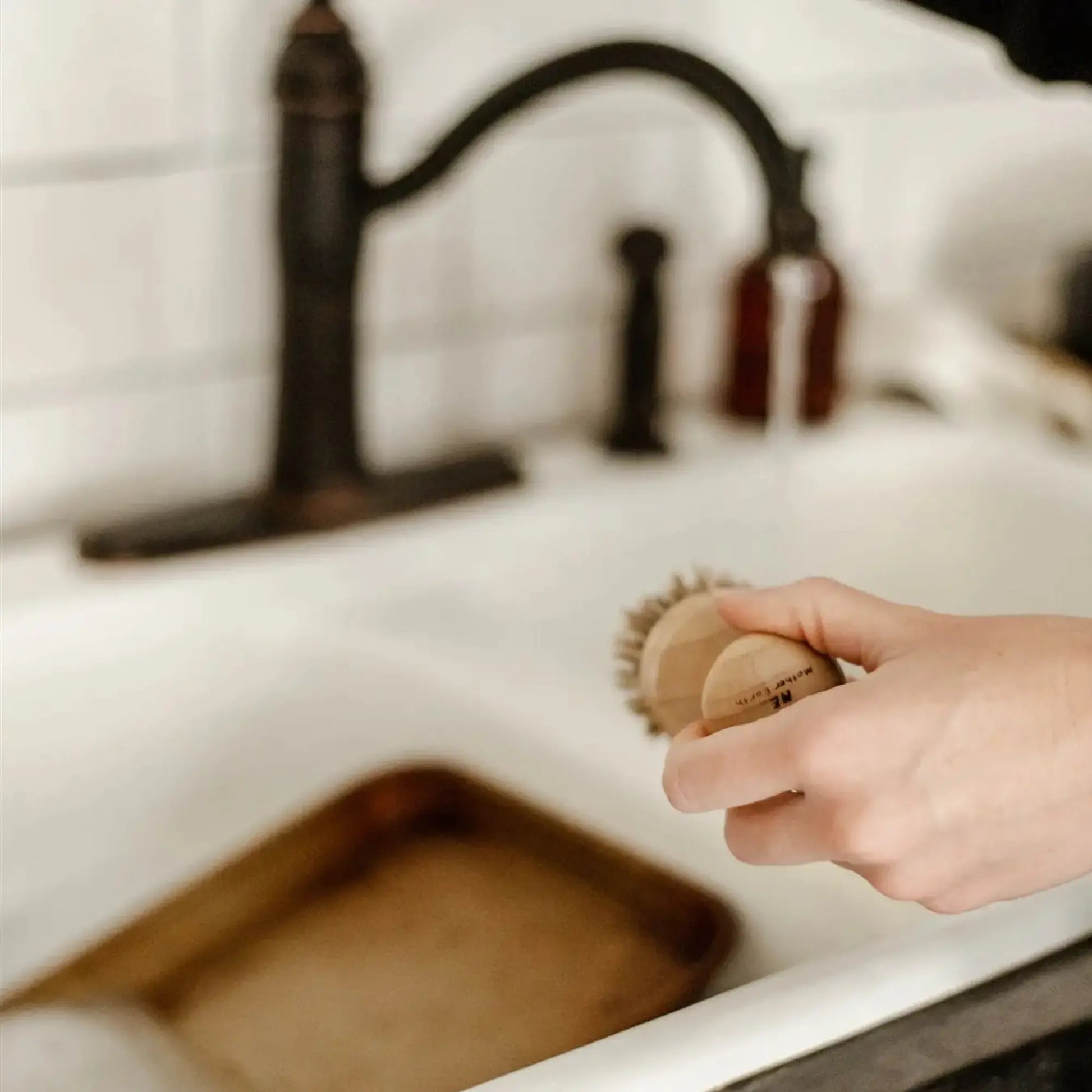 Person holding a scrubber over a sink with a blurred background