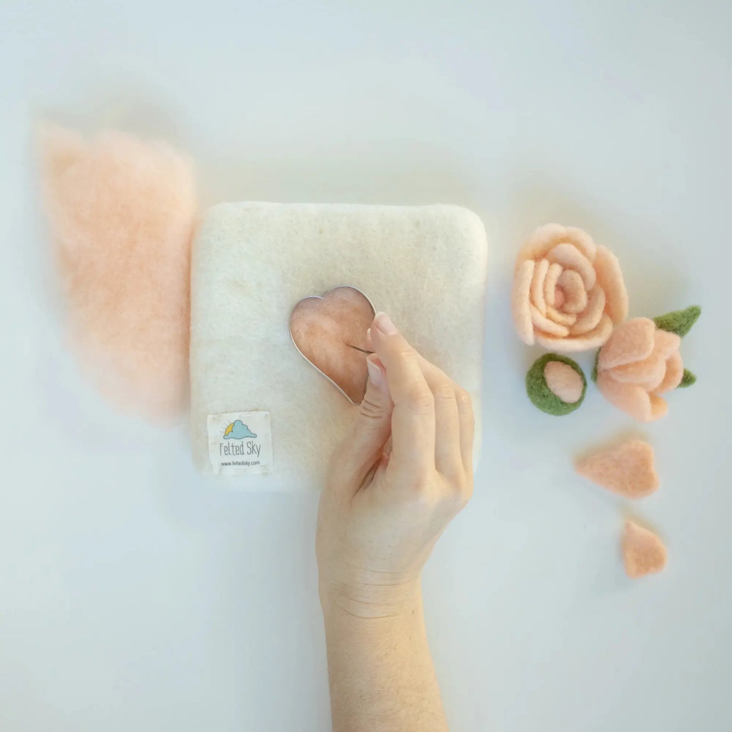 Hand needle felting a soft, peach-colored wool with decorative flowers on a light background