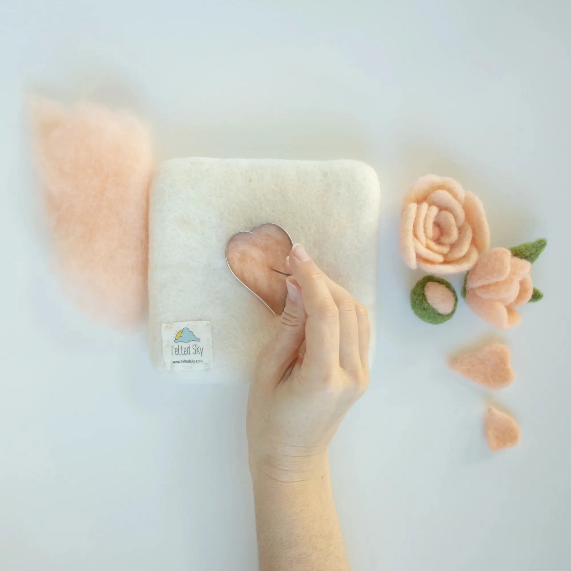 Hand needle felting a soft, peach-colored wool with decorative flowers on a light background