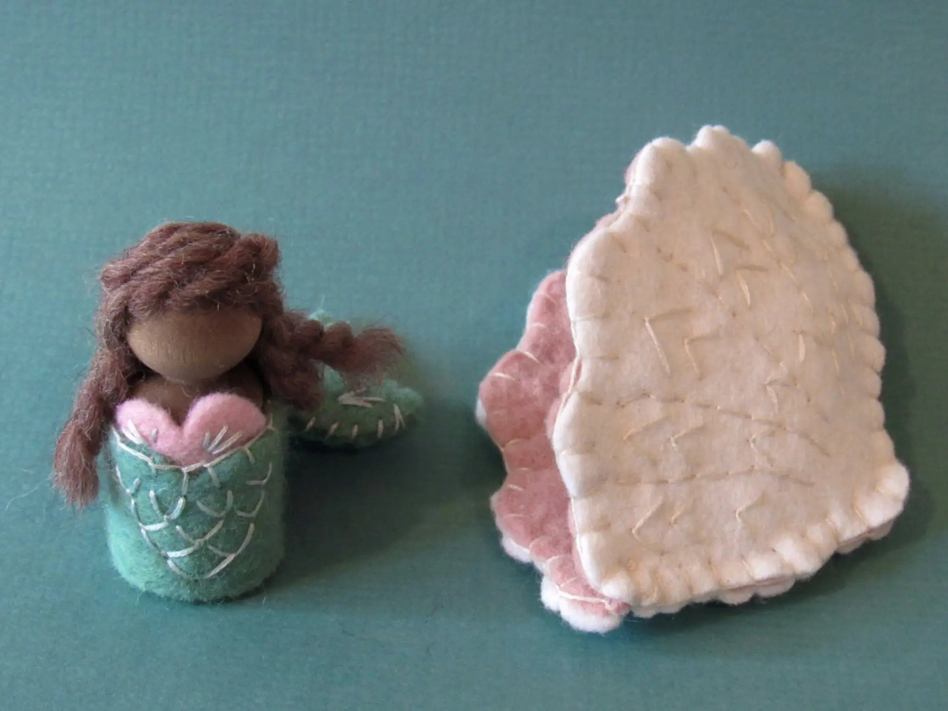 Mermaid figurine and shell on a teal background