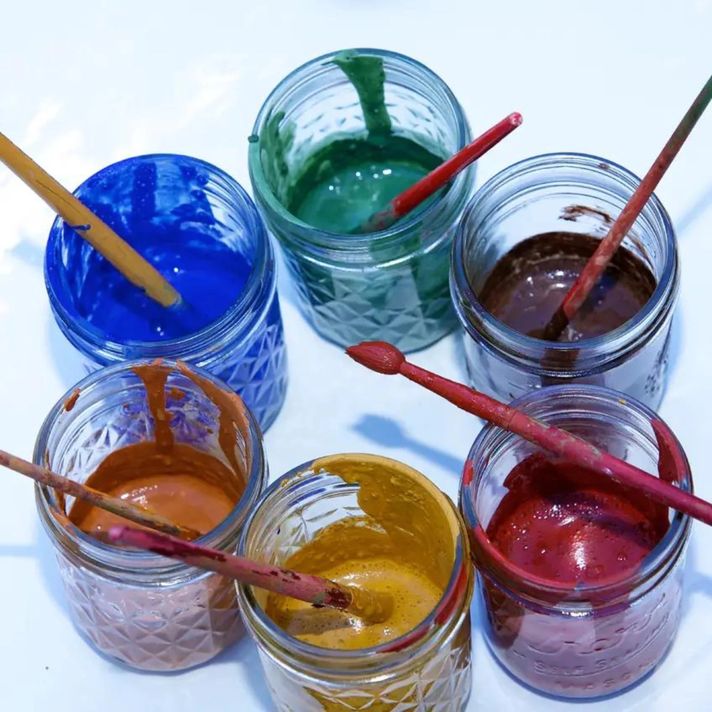 Six jars with colorful Kid friendly paint in mason jars and wooden paintbrushes on a white background