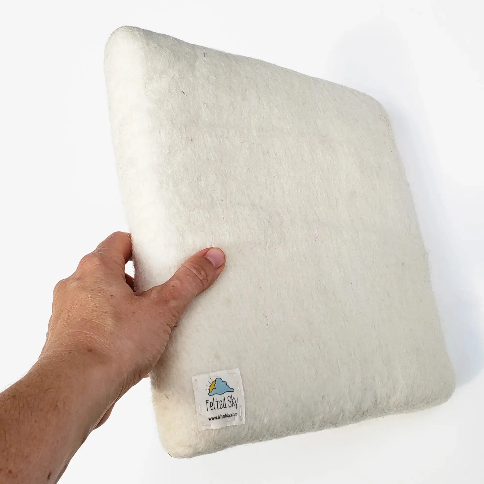 Hand holding a white wool needle felting mat with a label on a white background