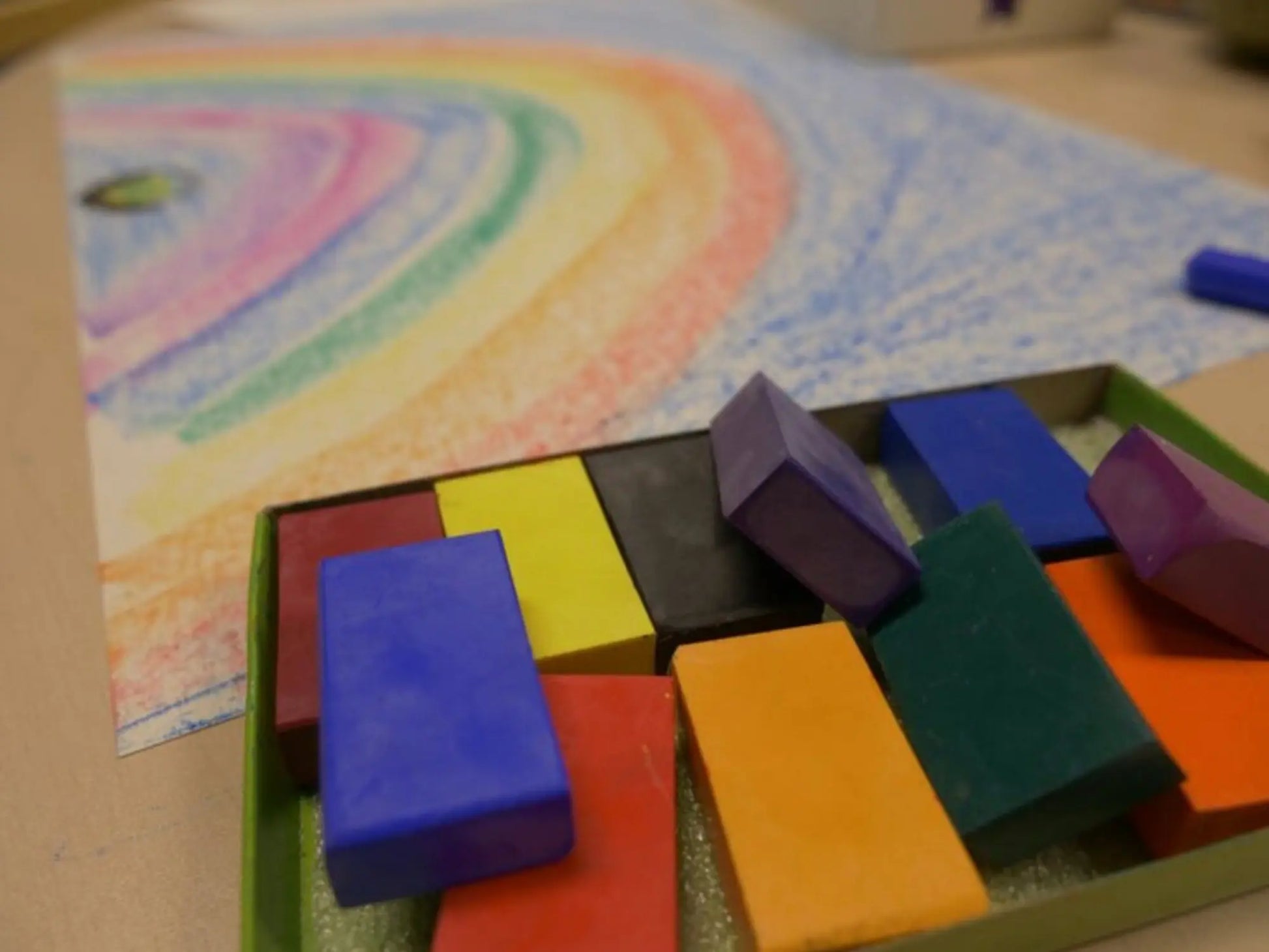 Colorful blocks in a box with a child's drawing of a rainbow in the background