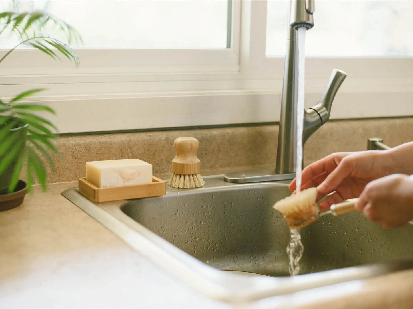 Person washing a sponge under running water in a kitchen sink.