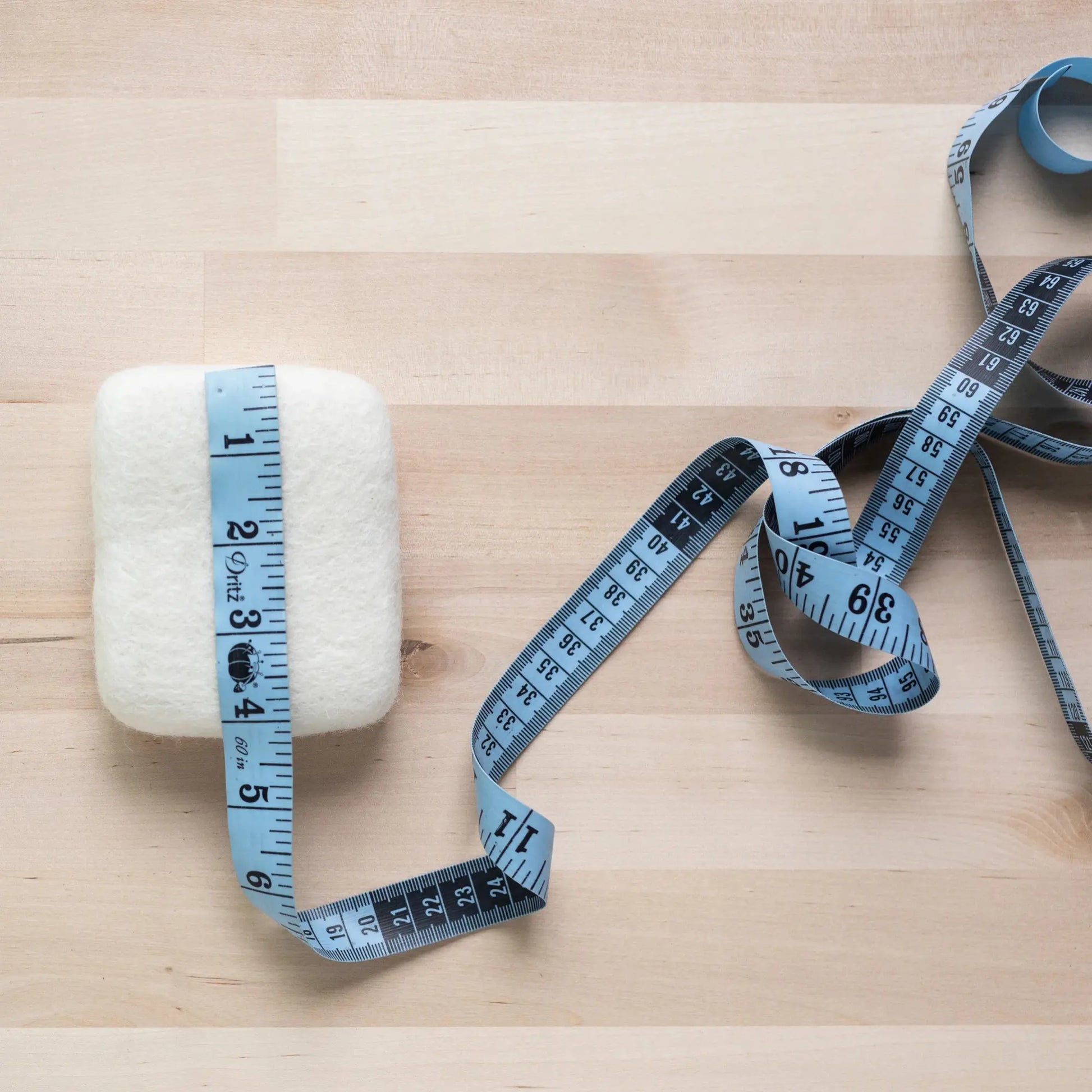 Measuring tape wrapped around an extra small needle felting mat made from wool