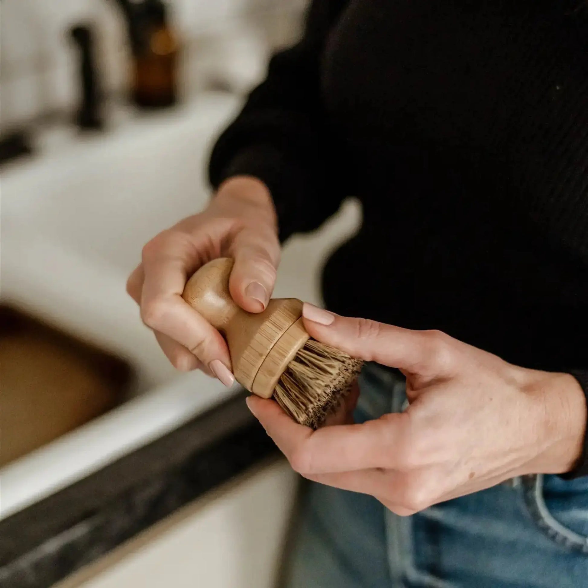 Person holding a wooden scrub brush in a kitchen setting