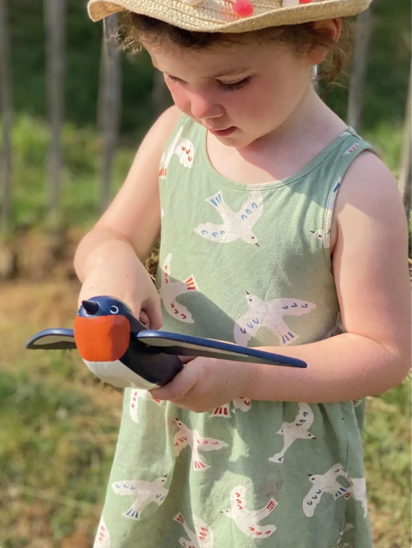 Child in a green dress with bird pattern holding a toy bird in an outdoor setting