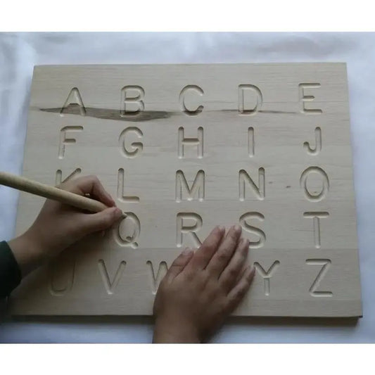 Wooden alphabet tracing board with hands using a wooden tool to press letters into the surface.