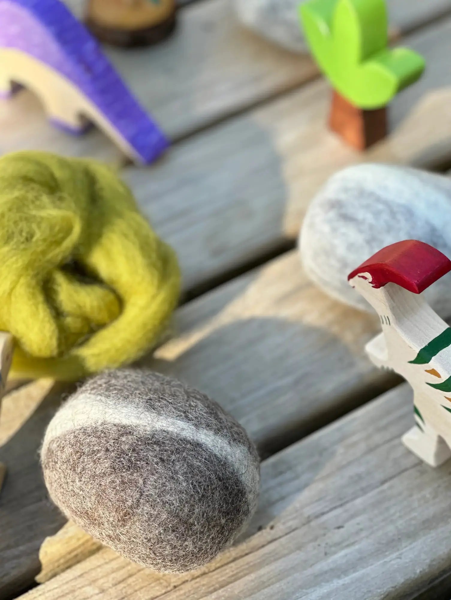 Felted balls on a wooden surface with colorful tools in the background