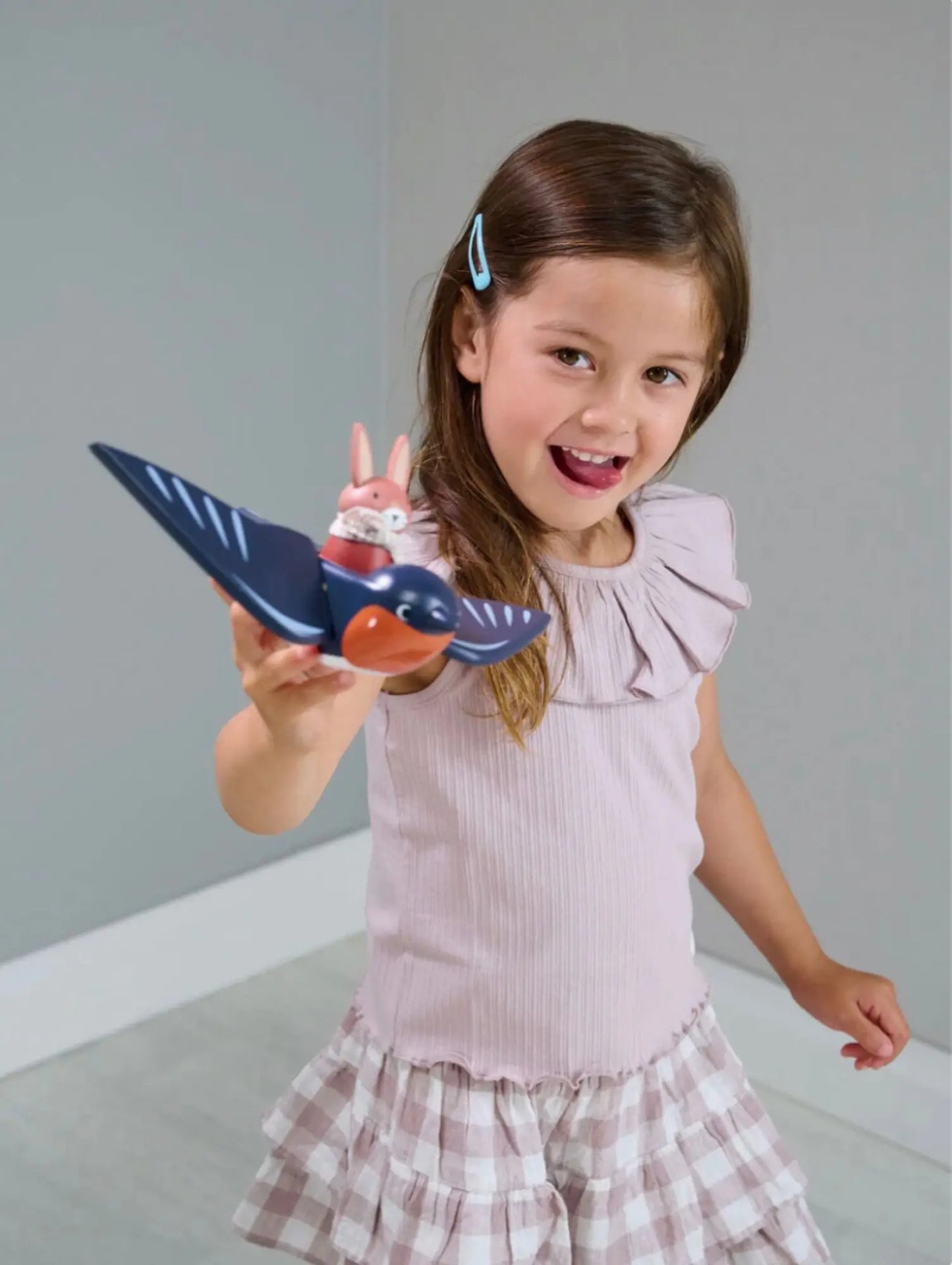 Young girl holding a toy tenderleaf wooden bird with hare against a plain background