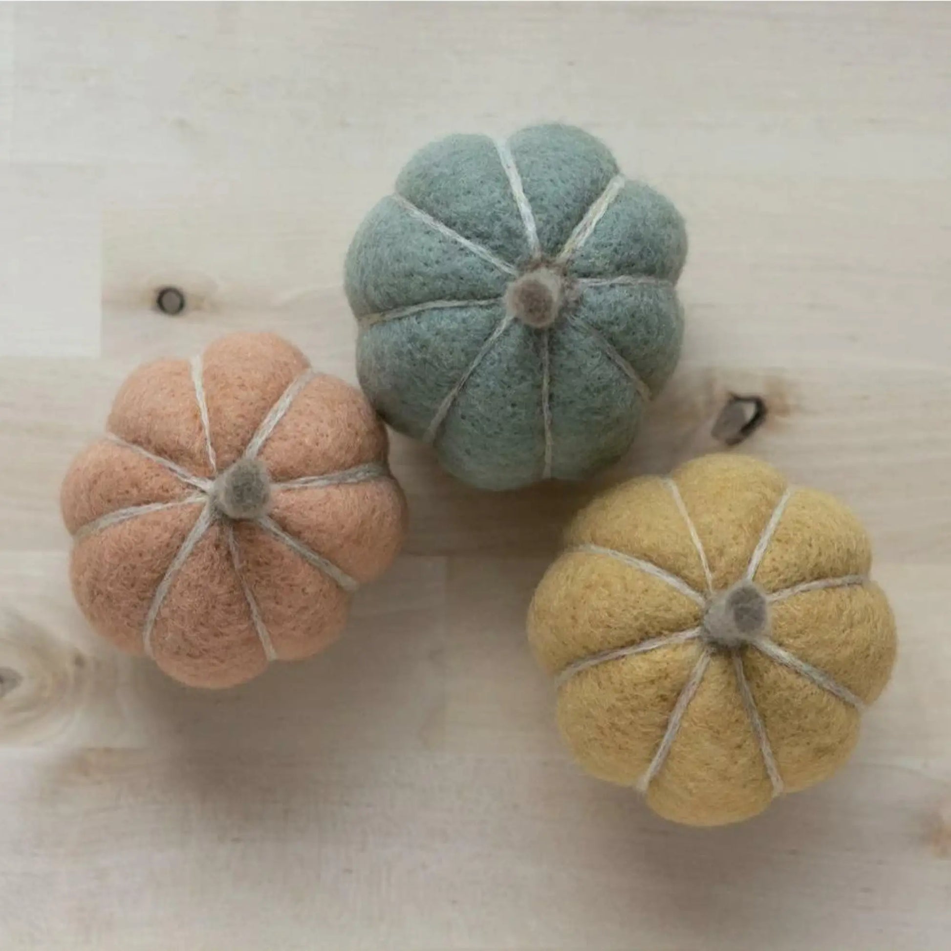 Three needle felted pumpkins in pastel colors on a wooden surface