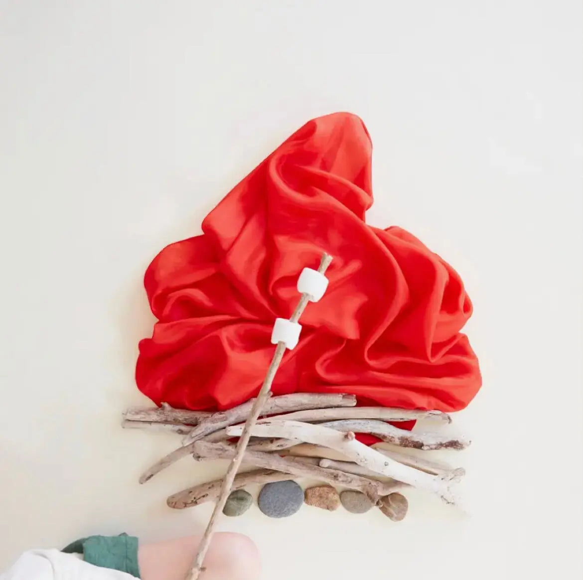Playsilk in Red arranged as pretend fire on sticks with a child holding marshmallows