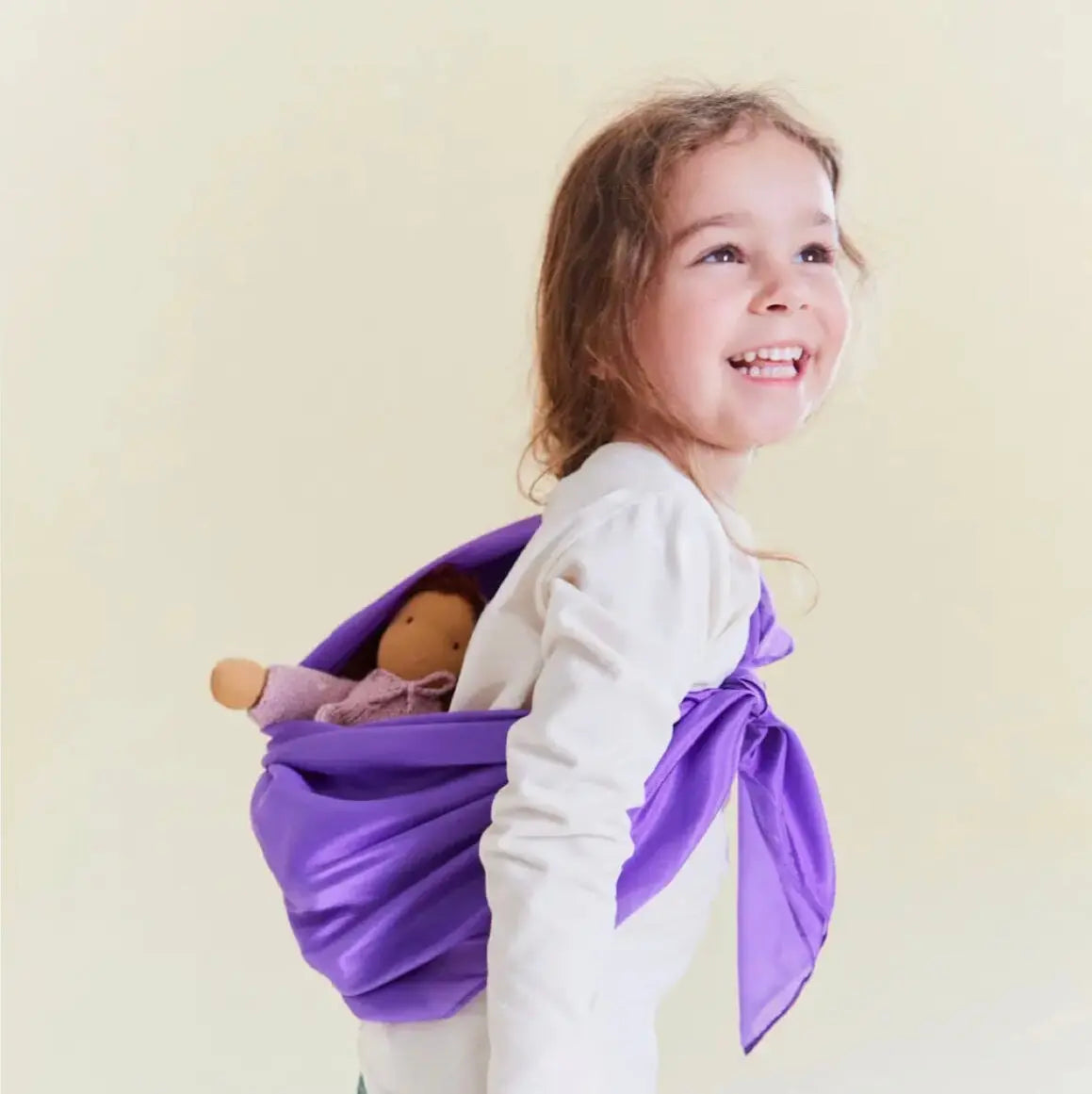 Girl with purple playsilk tied to her back as a doll sling with a doll inside