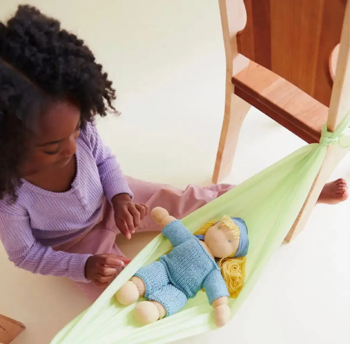 Girl playing with a doll with playsilk tied to chairs to make a doll bed