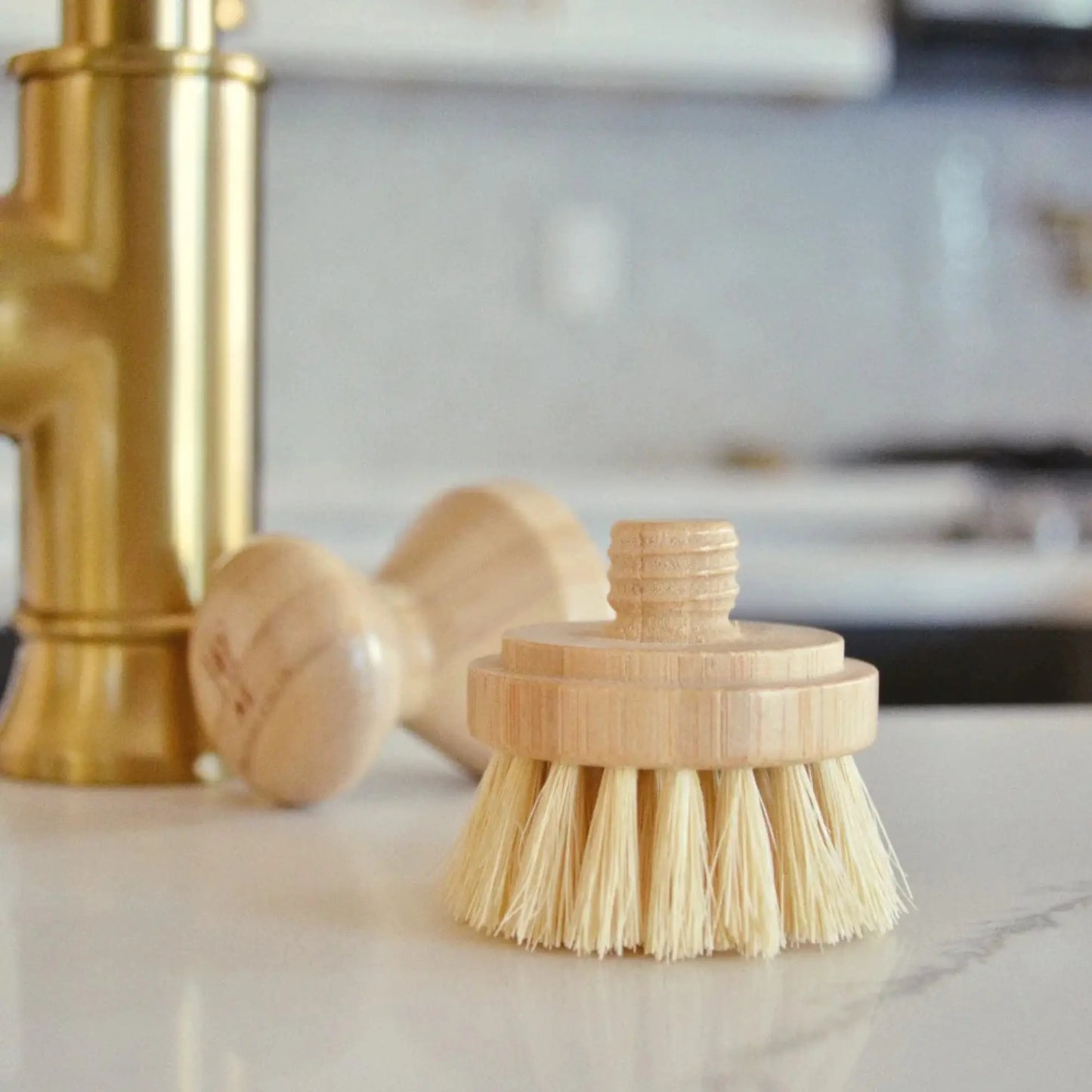 Wooden dish brush with bristles on a kitchen counter next to a gold faucet.