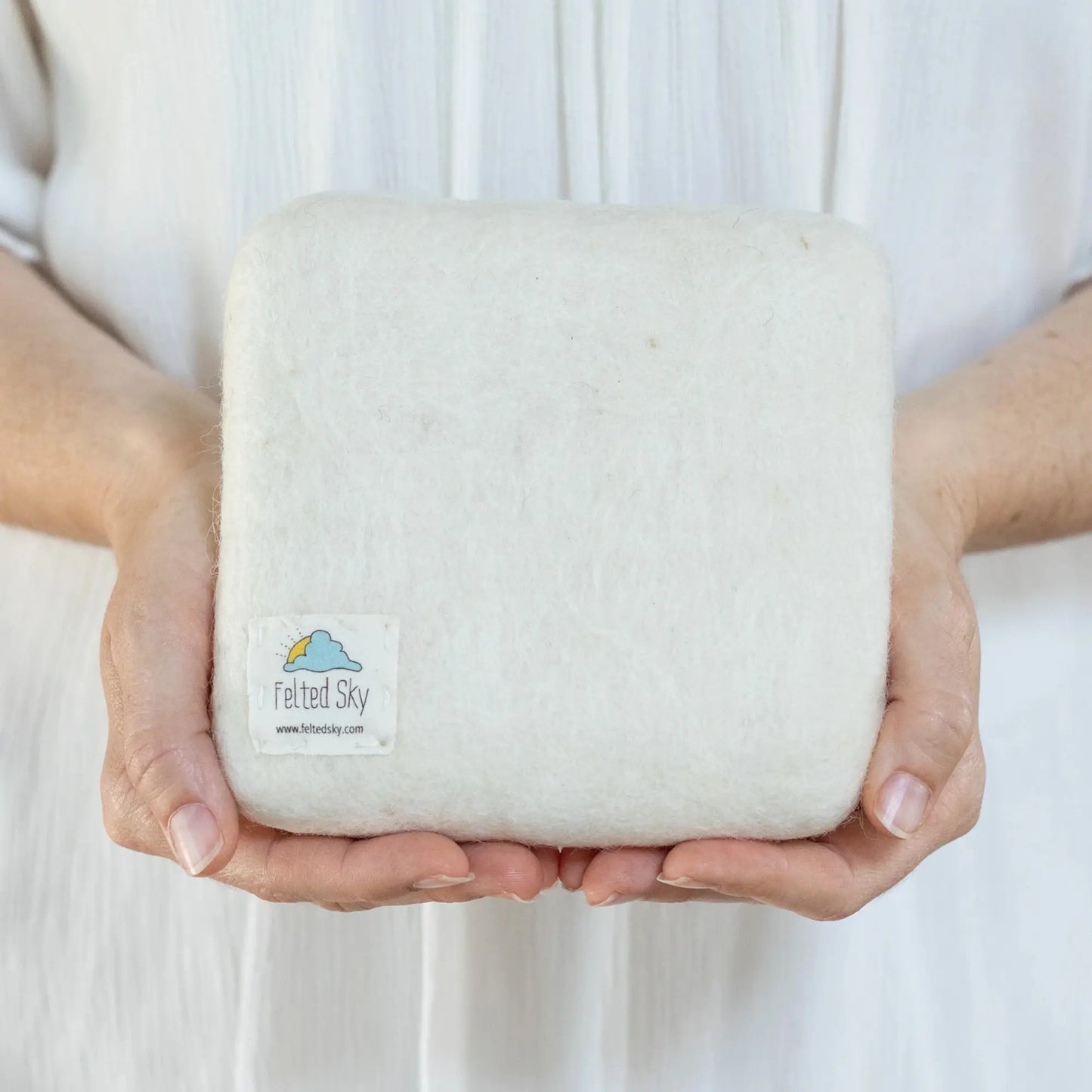 Person holding a medium needle felting mat with 'Felted Sky' branding against a white background