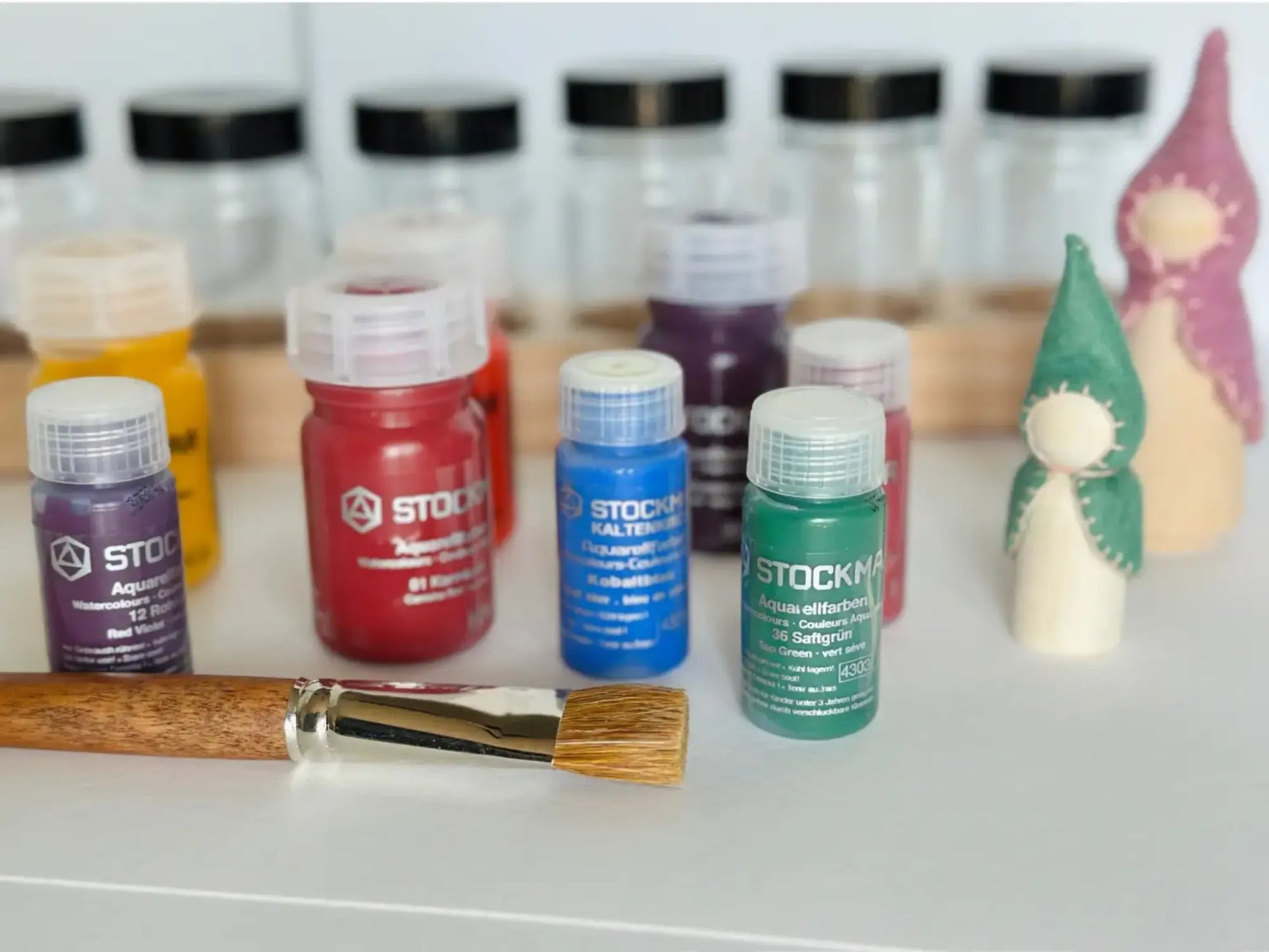 Set of Stockmar watercolor paint bottles with a brush on a white surface.
