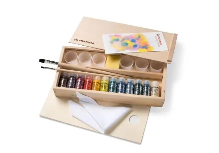 Wooden art supply set with Stockmar paint bottles, brushes, and a palette on a white background