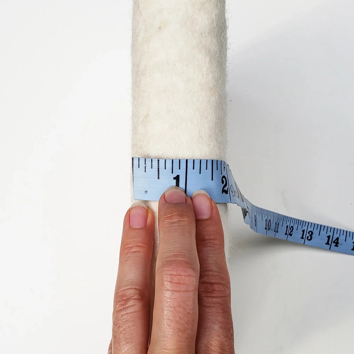 Hand holding a measuring tape against a needle felting mat to show thickness of over 1.5"