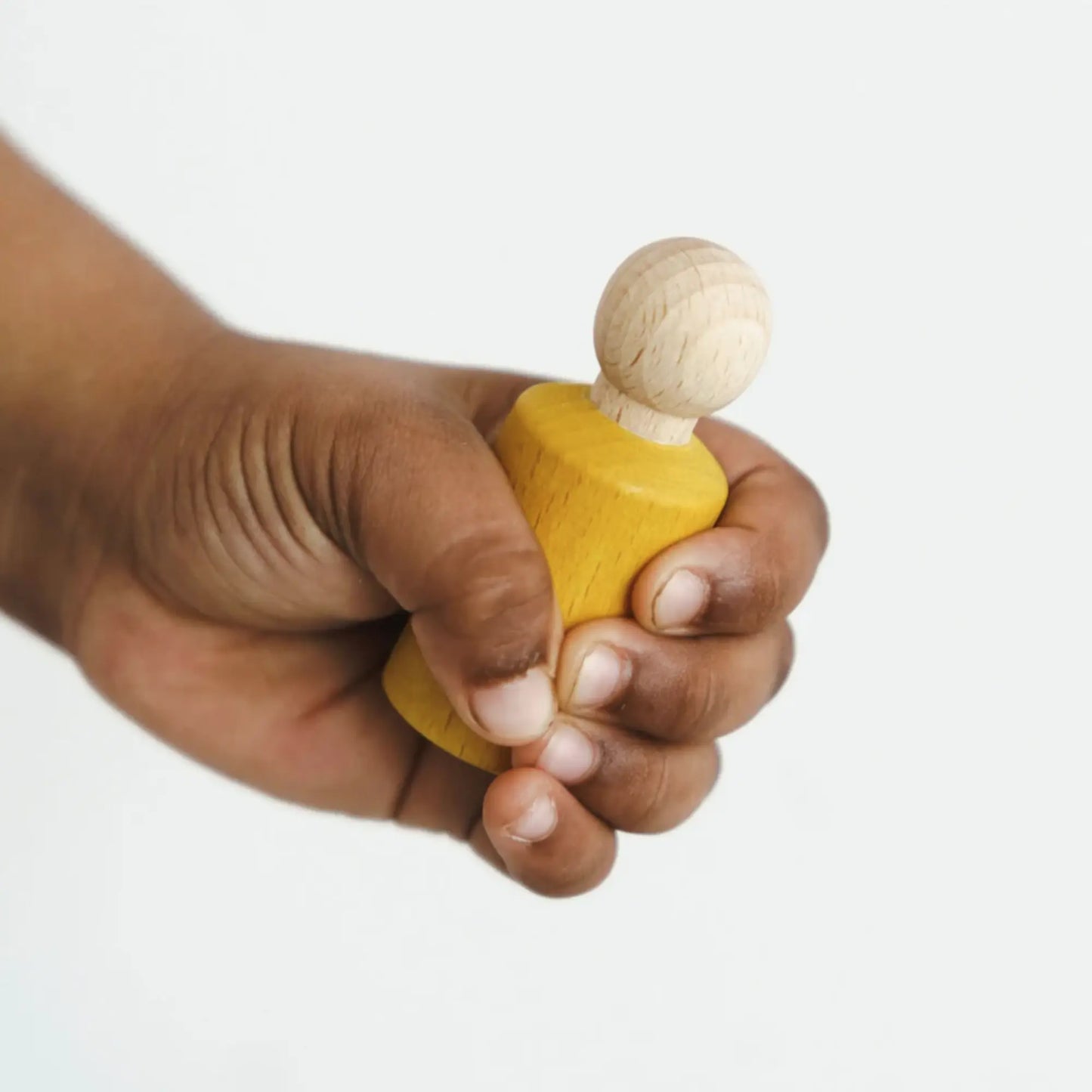 Hand holding a small blue jWaldorf inspired Yellow stained peg doll  against a white background