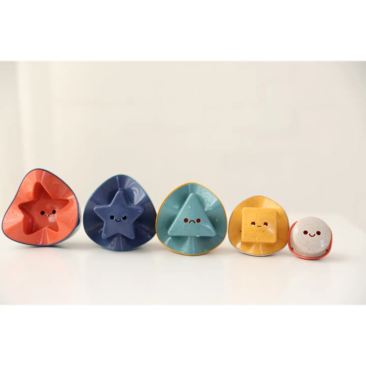 Five colorful sand and water stacking toys with facial expressions on a light background