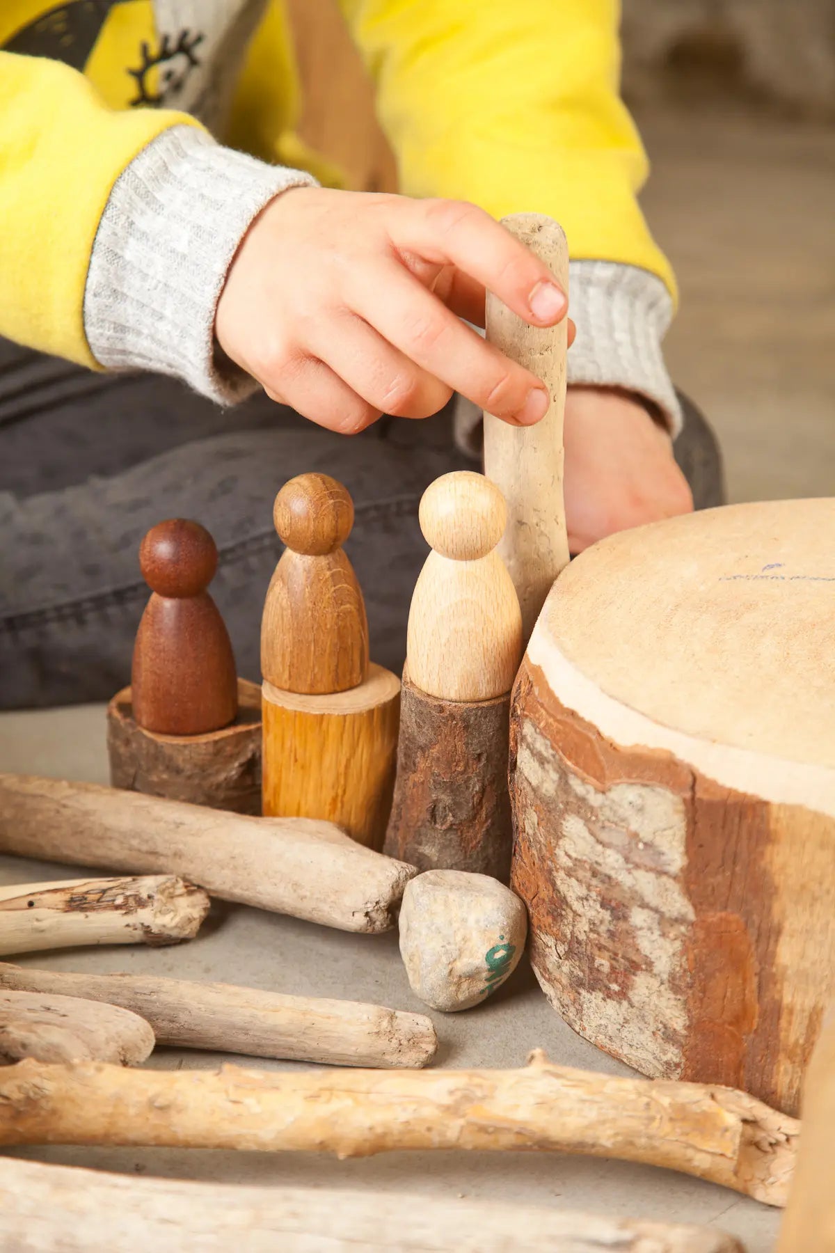 Child playing with wooden Grapat toys called Nins on a tree stump surface