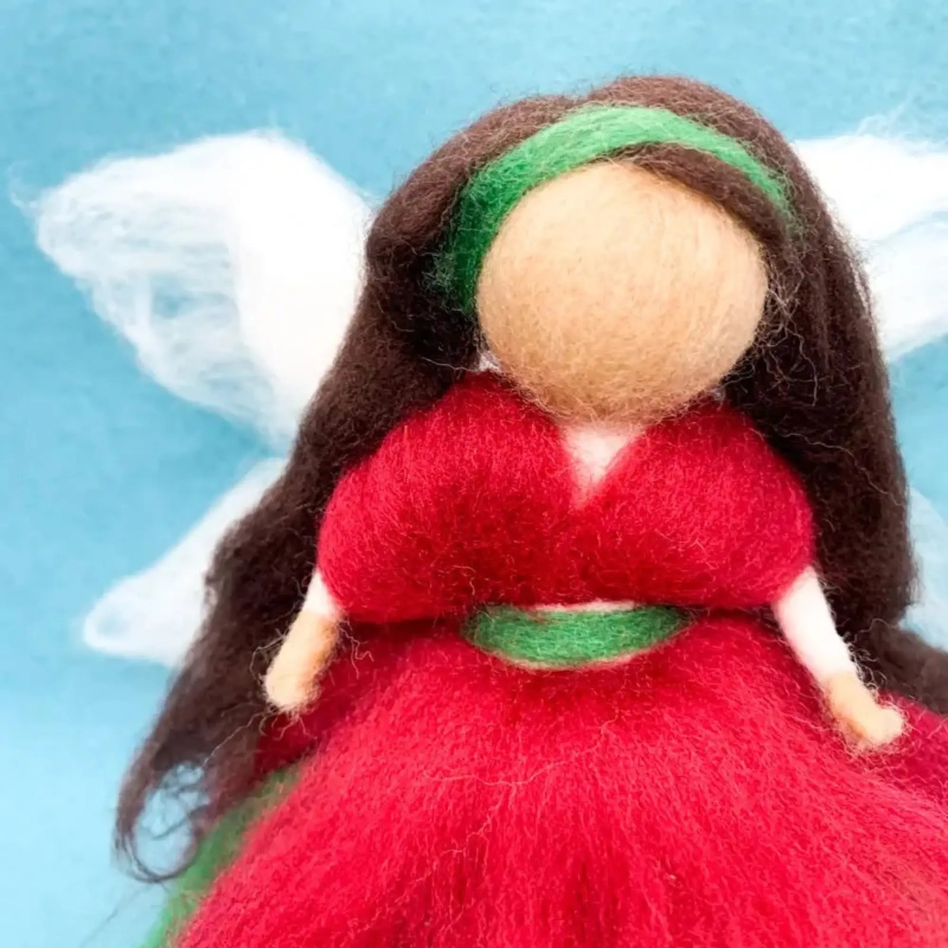 Felted angel doll with red dress and green headband on a blue background