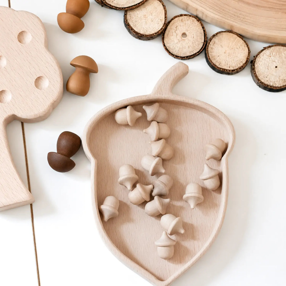 Acorn-shaped wooden nature table tray filled with small wooden acorns, surrounded by wood slices and natural loose parts.