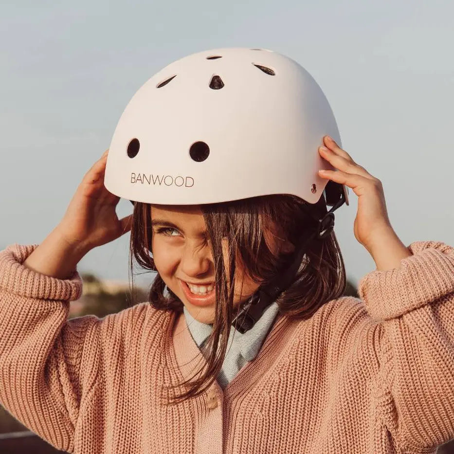 Child wearing a white bike helmet with 'Banwood' branding, smiling outdoors.