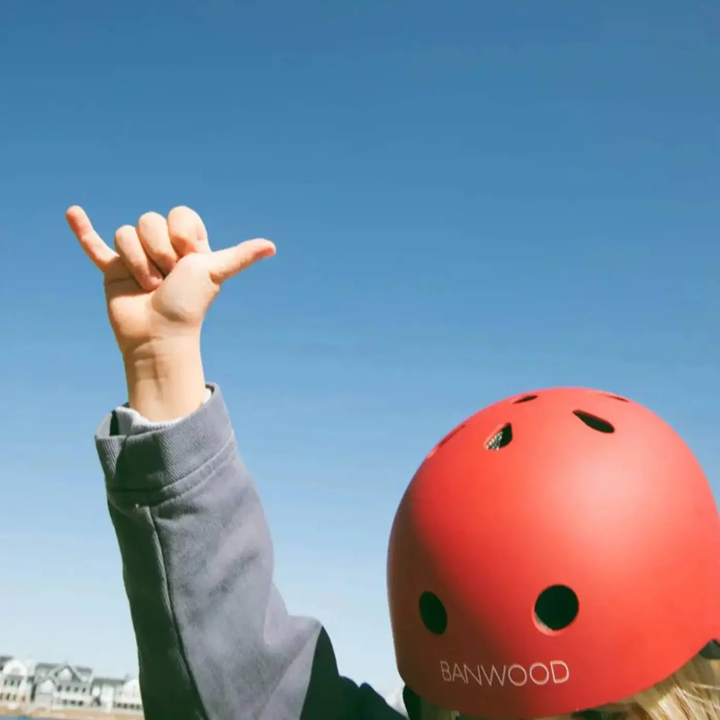 Person wearing a red bike helmet with Banwood branding against a clear blue sky.